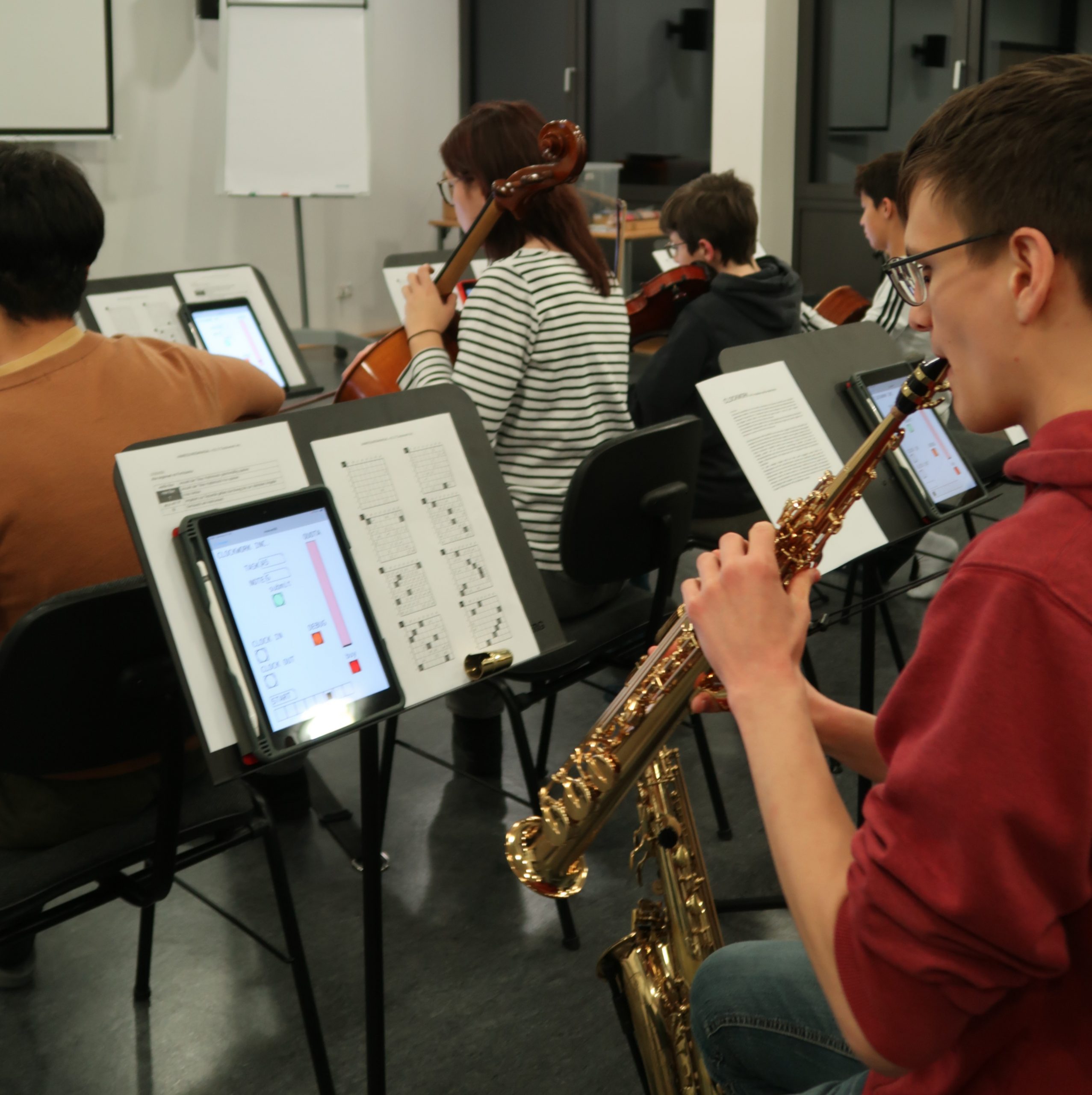Jugendliche spielen mit ihren Instrumenten von Notenständern, auf denen Tablets und Spielanweisungen liegen